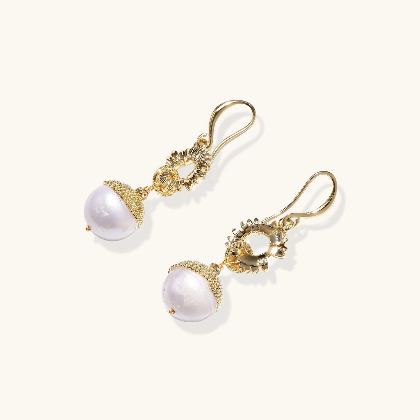 Gold-plated sunburst flower earrings with baroque pearl drops and textured metal caps on neutral background.