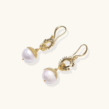 Gold-plated sunburst flower earrings with baroque pearl drops and textured metal caps on neutral background.