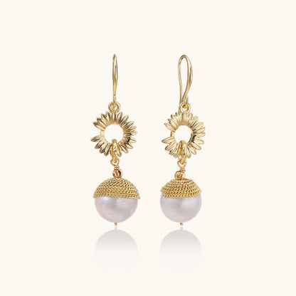 Gold-plated sunburst flower earrings with baroque pearl drops and textured metal caps on neutral background.