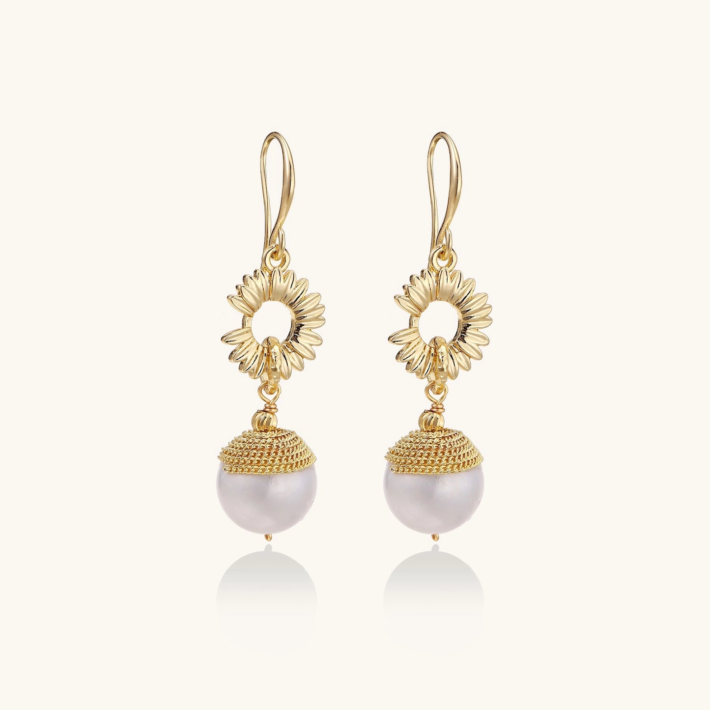 Gold-plated sunburst flower earrings with baroque pearl drops and textured metal caps on neutral background.