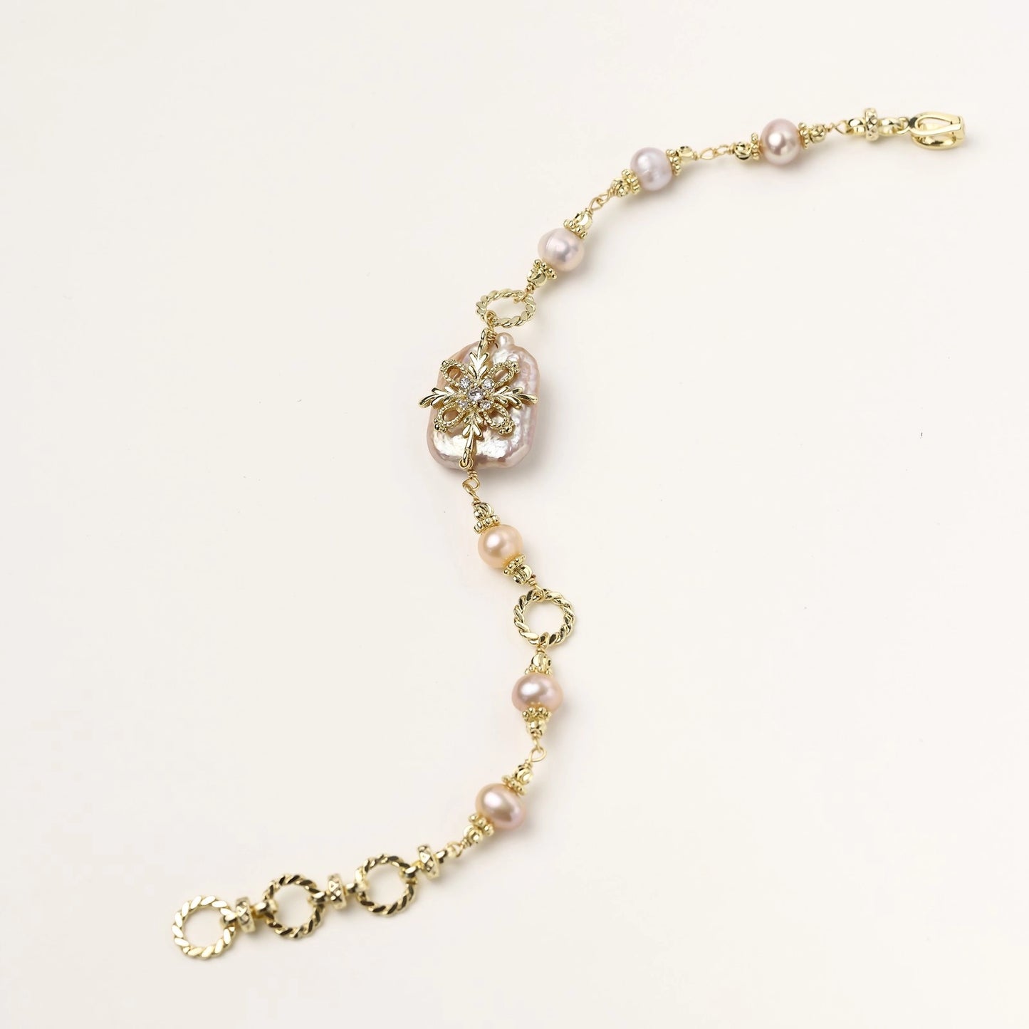 Gold-plated chain bracelet with baroque pearl centerpiece and floral charm, featuring mixed freshwater pearls.