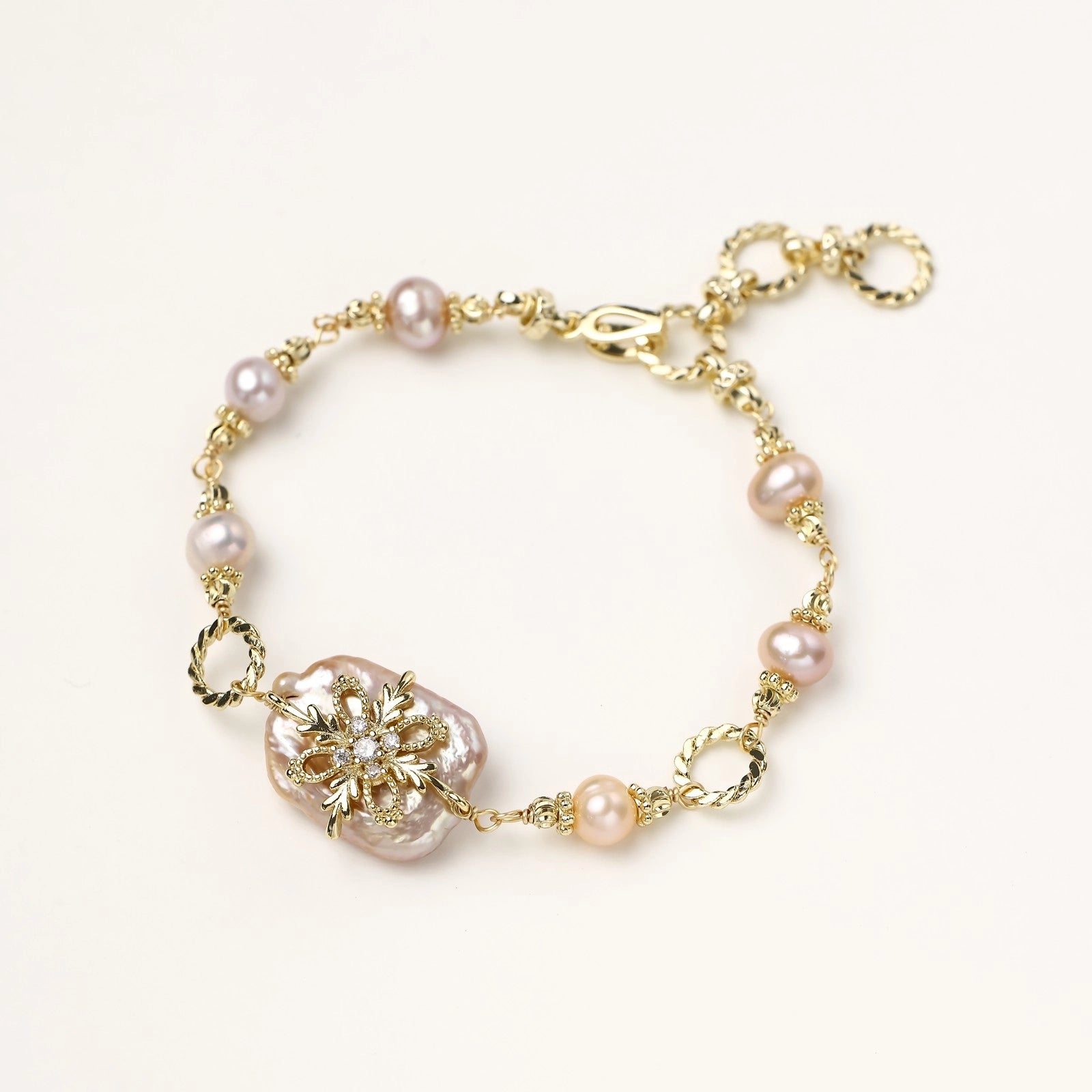 Gold-plated chain bracelet with baroque pearl centerpiece and floral charm, featuring mixed freshwater pearls.