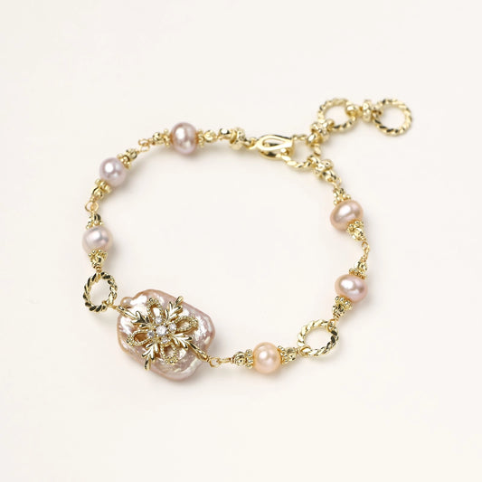 Gold-plated chain bracelet with baroque pearl centerpiece and floral charm, featuring mixed freshwater pearls.