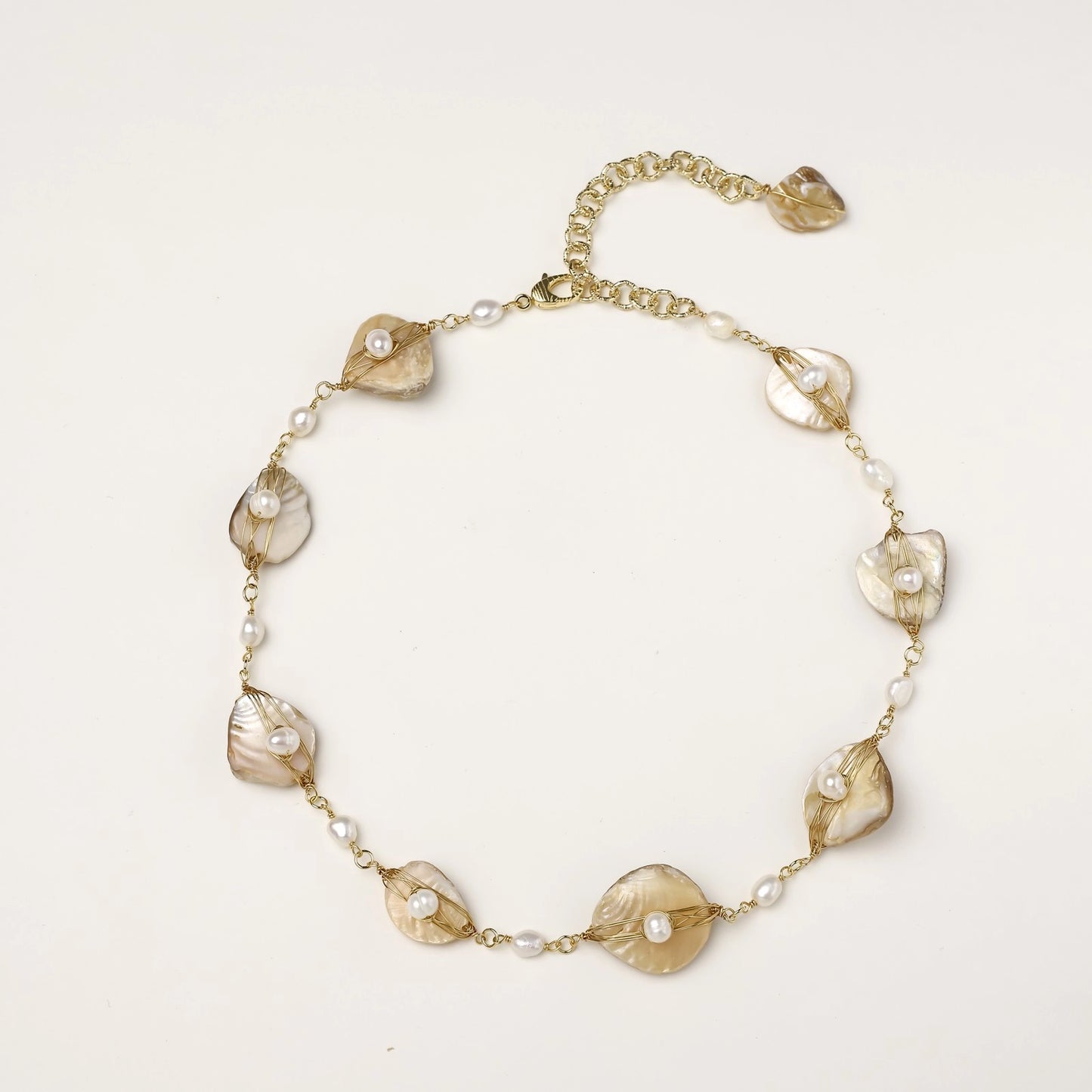 Elegant gold-plated necklace with organic shell leaf elements each holding a freshwater pearl on neutral background.