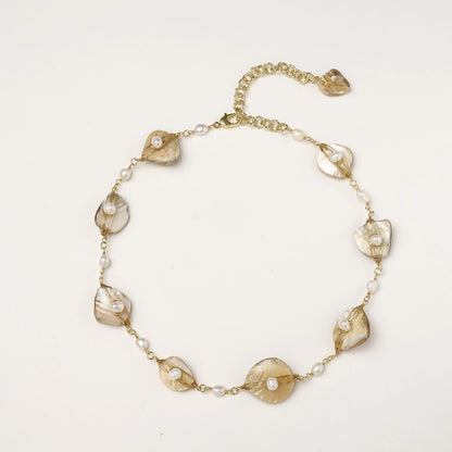 Elegant gold-plated necklace with organic shell leaf elements each holding a freshwater pearl on neutral background.