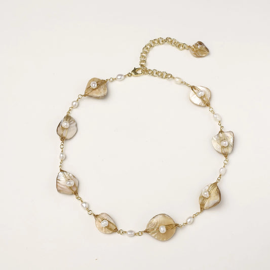 Elegant gold-plated necklace with organic shell leaf elements each holding a freshwater pearl on neutral background.