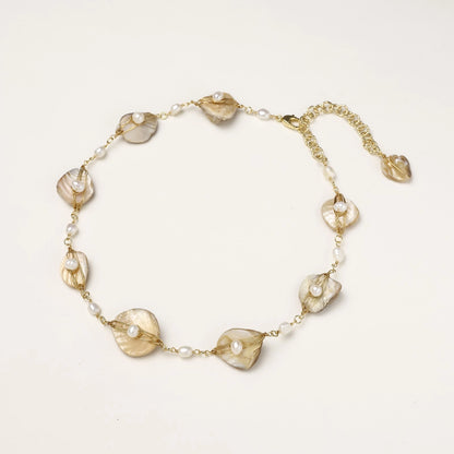 Elegant gold-plated necklace with organic shell leaf elements each holding a freshwater pearl on neutral background.