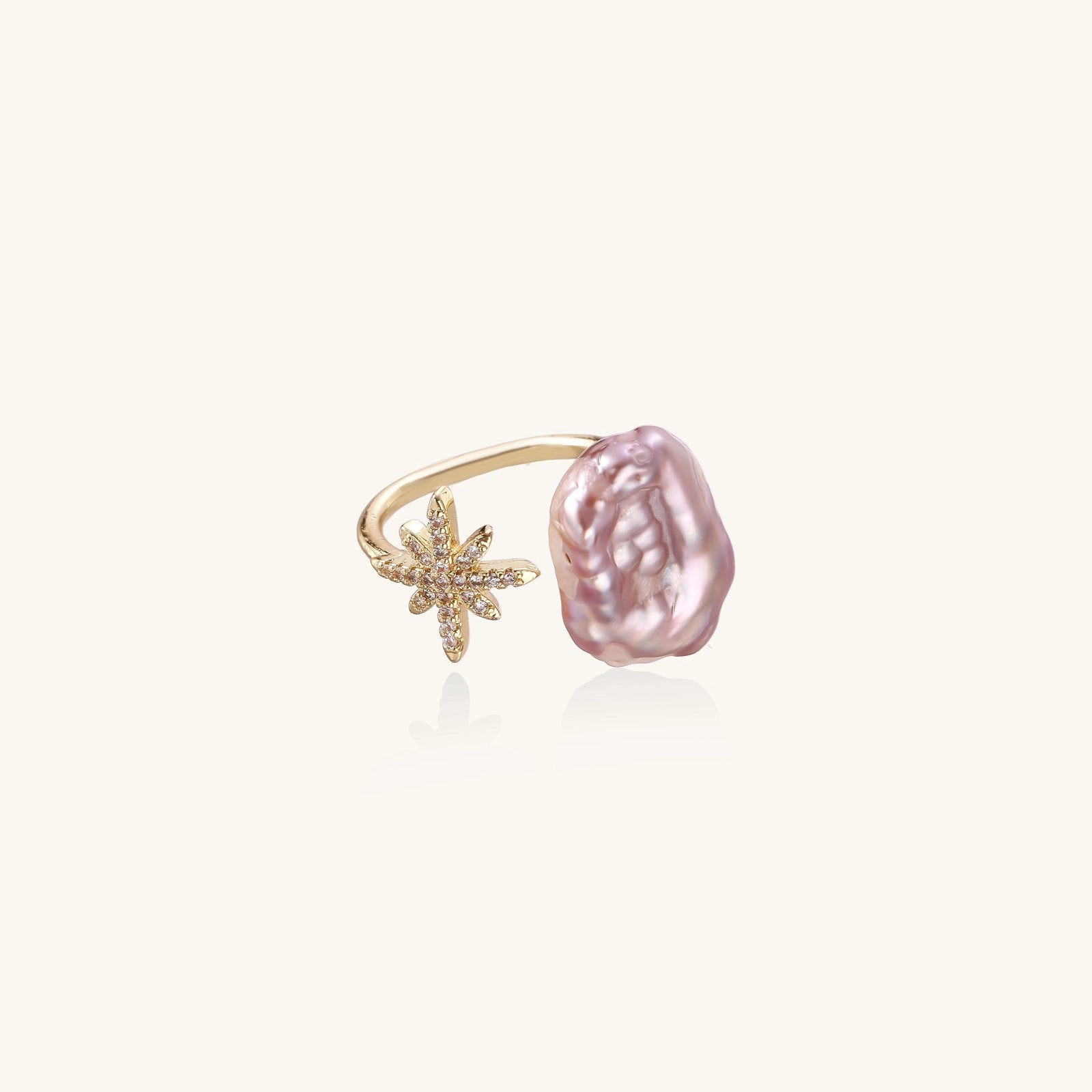 Adjustable ring with lavender baroque pearl and crystal star charm on gold-plated band against cream background.