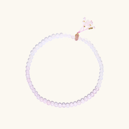 Stretchable bracelet with pink rose quartz and white agate beads, featuring a decorative tassel pendant on white background.
