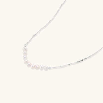 Delicate sterling silver chain with small white freshwater pearls arranged asymmetrically on white background.