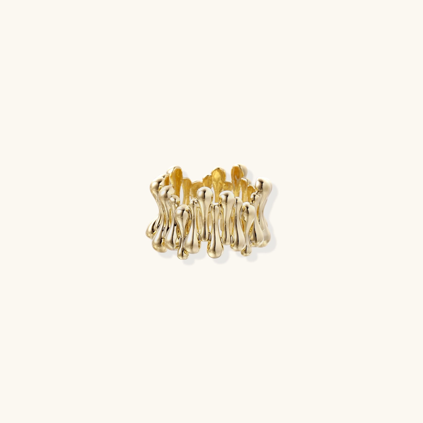 Close-up of chunky 18K gold-plated brass ring with flowing wave-like sculptural design on neutral background.
