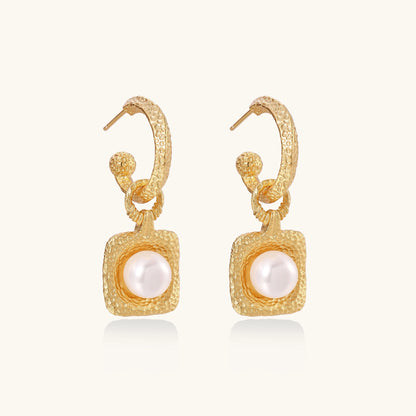 Gold-plated textured hoop earrings with square pendants containing freshwater pearls on white background