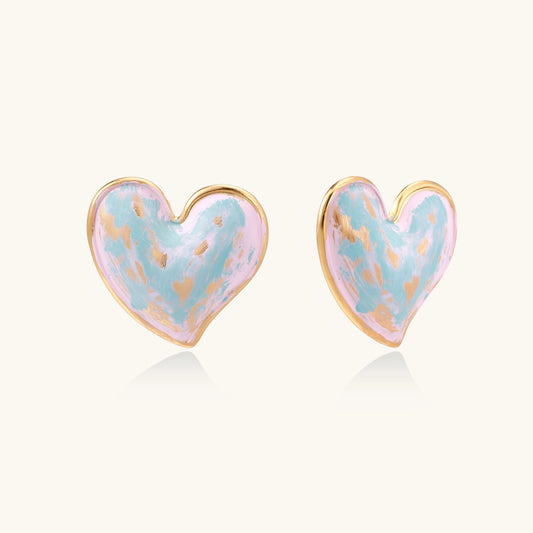 Heart-shaped stud earrings with iridescent blue-pink enamel finish and gold-plated brass frames against cream background