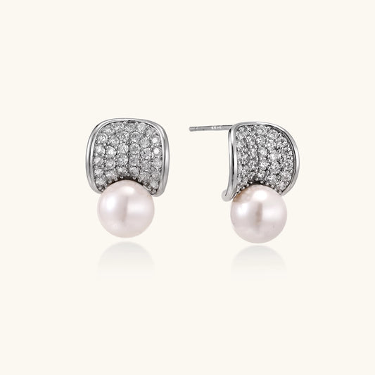 Elegant gold-plated curved earrings with diamond pavé crescents and suspended freshwater pearls on neutral background.