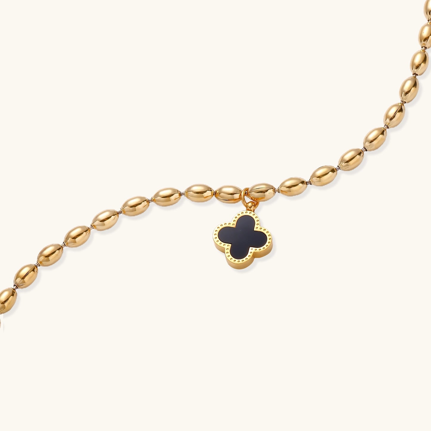 Dainty gold-plated beaded bracelet with oval links and four-leaf clover charm pendant on neutral background.